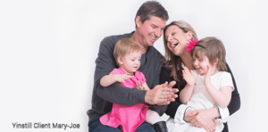 A joyful family moment with two adults and two young children, sharing laughter and playful interaction against a bright background.