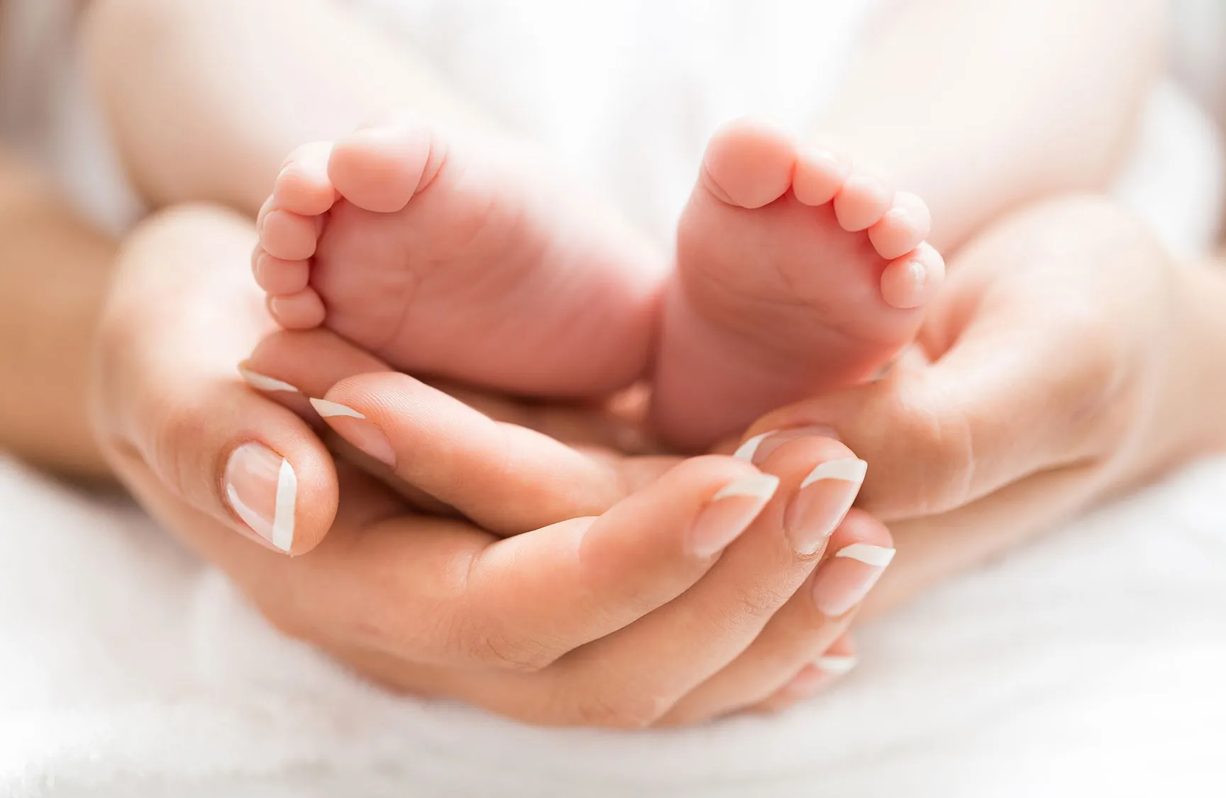 A close-up of a pair of baby feet resting in an adult's hands, symbolizing care and tenderness.