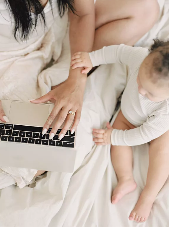 A parent works on a laptop while a child reaches out from beside them, creating a warm and nurturing atmosphere.